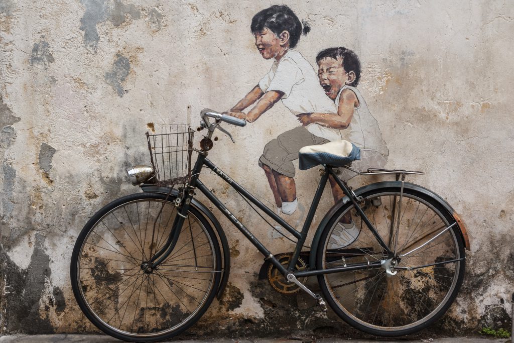 กำแพงที่มีจักรยานพิงอยู่พร้อมกับภาพเขียนเด็กสองคนที่ทำเหมือนกำลังปั่นจักรยาน